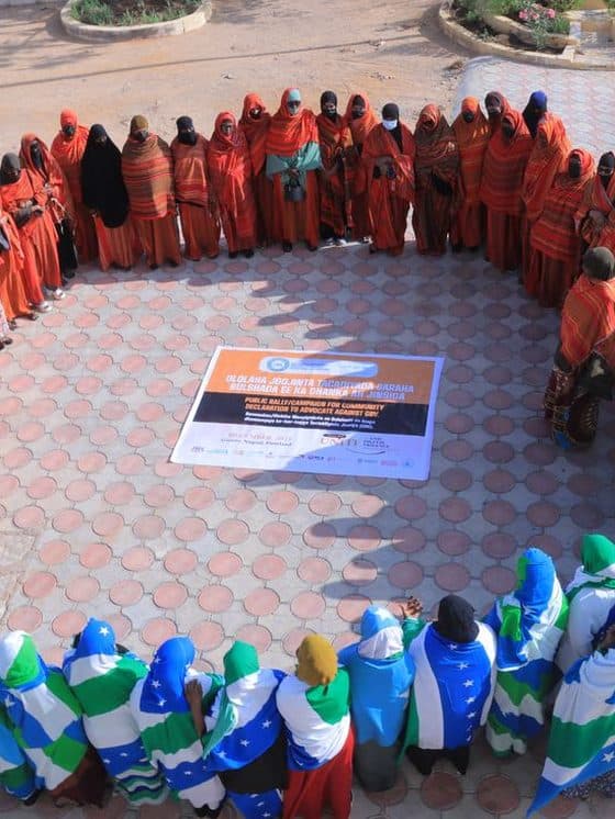 Women forming a circle around a public declaration banner against GBV